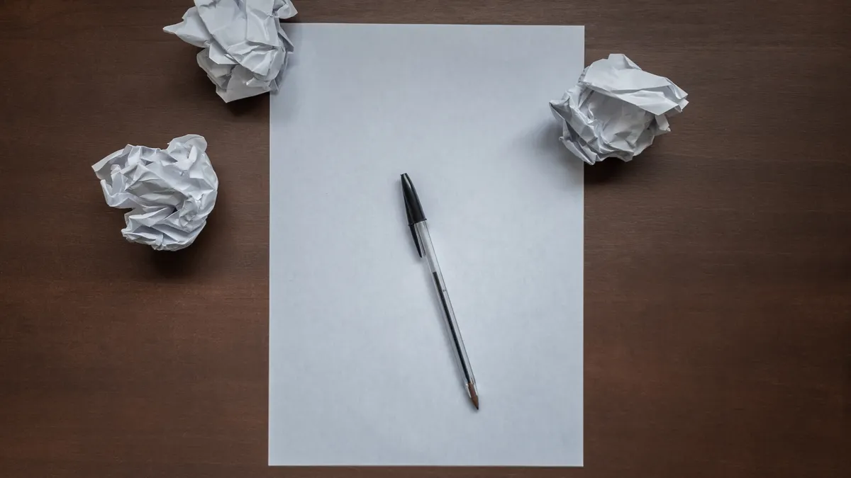 Jasper vs Copy.ai for marketing copy — Flat lay with blank writing sheet, pen and crumpled paper balls on top of wooden 